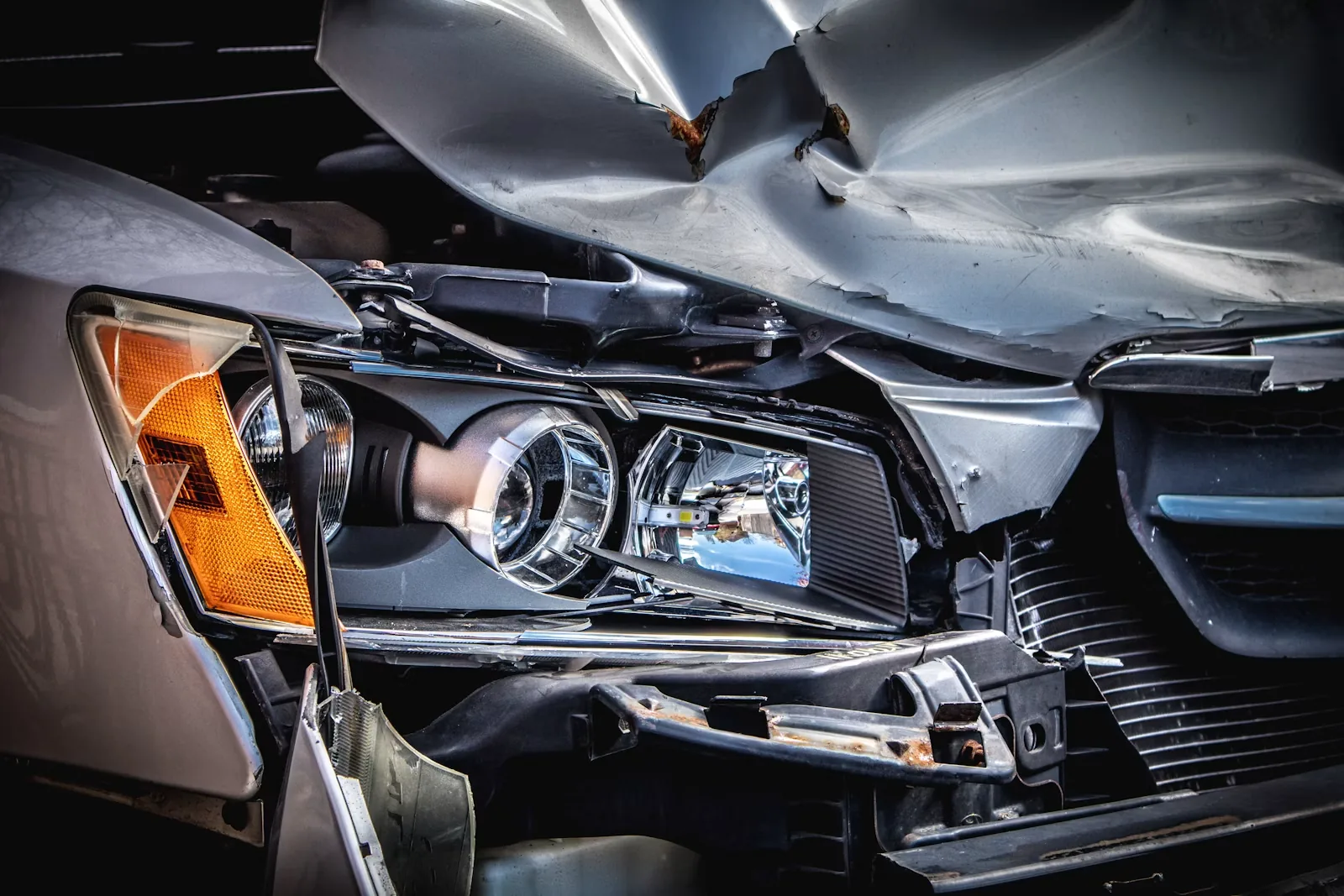 Damaged silver car with a crushed hood and broken headlight after a collision