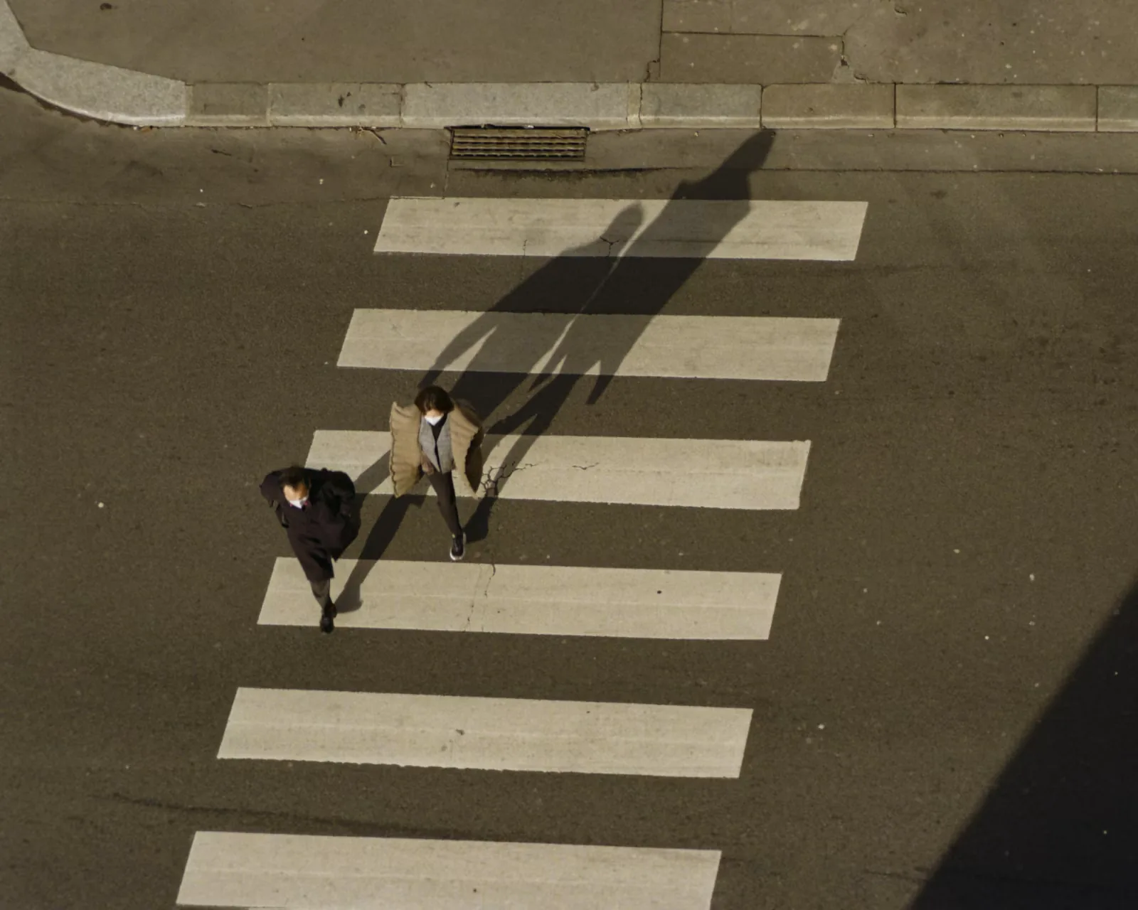 A man and a woman walking across a marked crosswalk in the city
