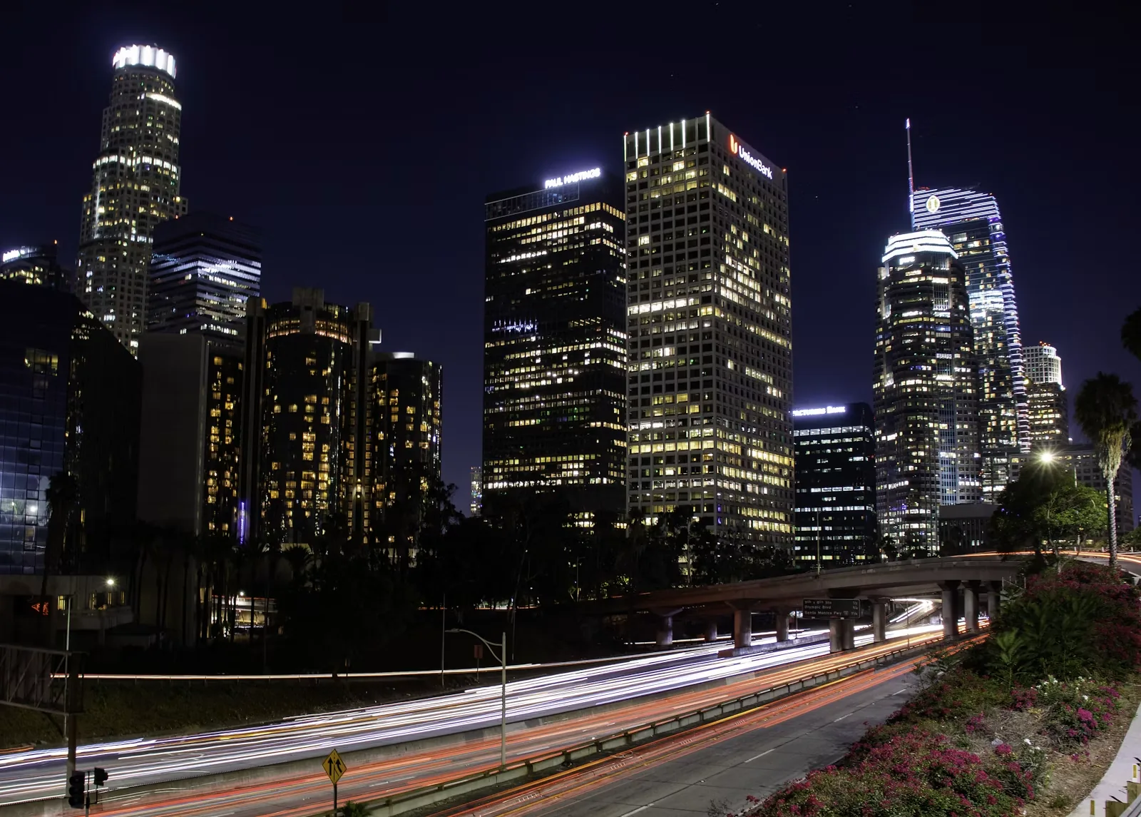 City skyline at night with car lights streaking along the road