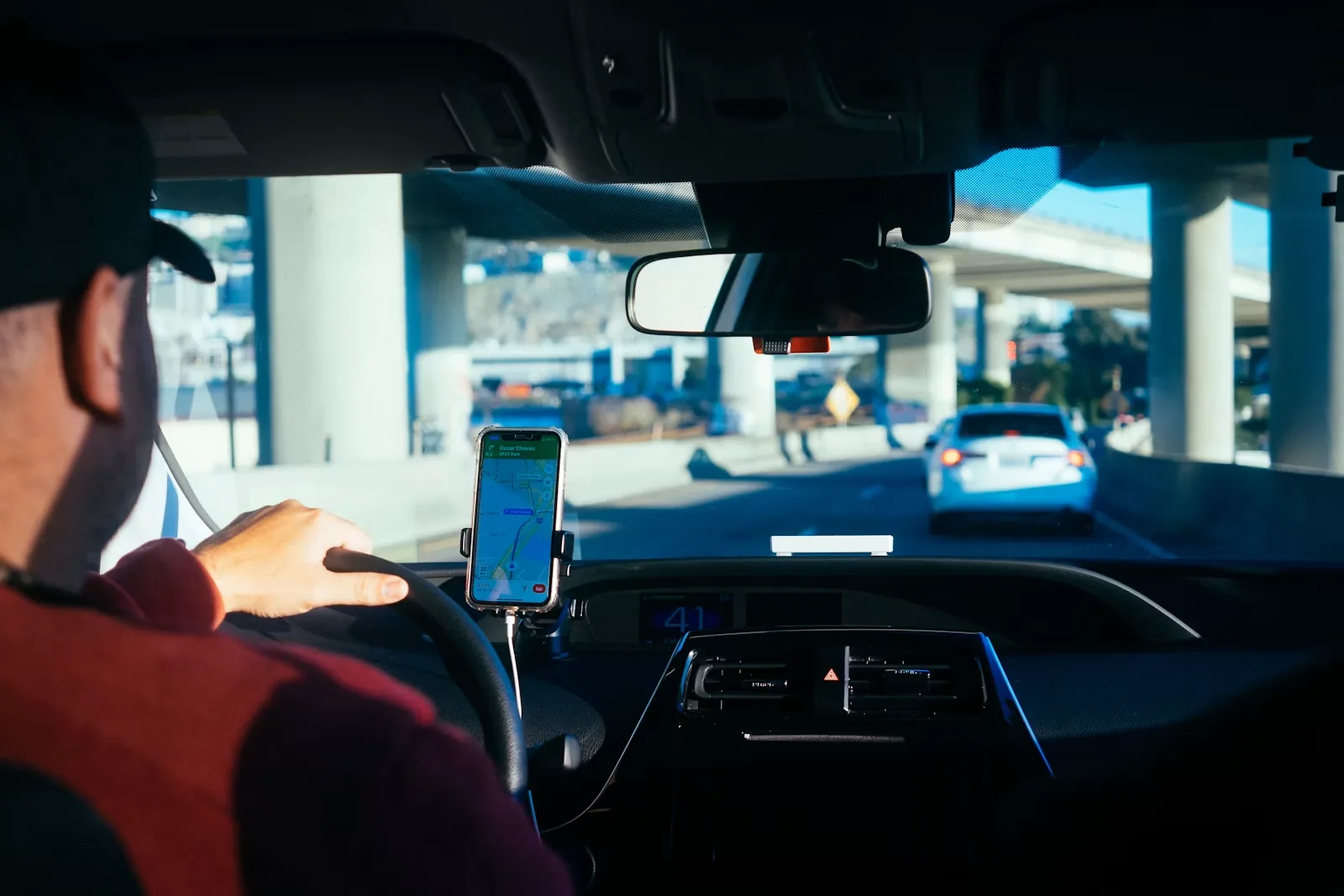 Driver behind the wheel with a smartphone navigation app mounted on the dashboard